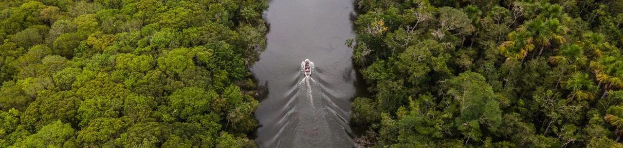Vista aérea de um barco navegando por um rio entre a mata fechada do Jardim da Amazônia Lodge