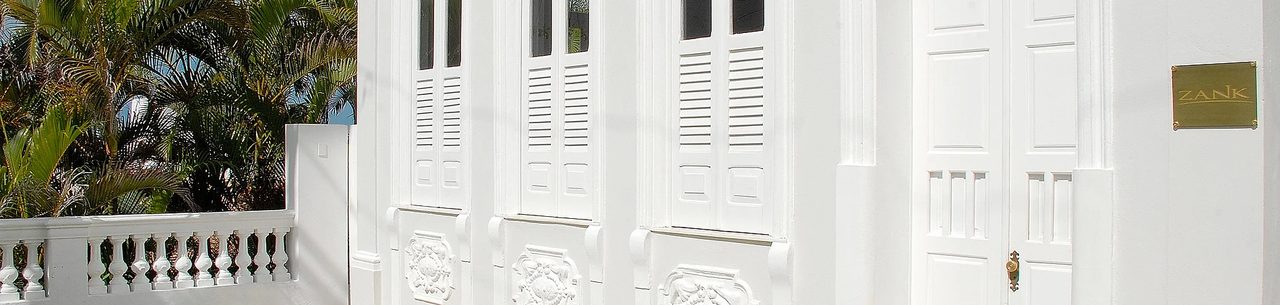 Fachada branca do casarão do Zank Hotel Boutique, com venezianas, ornamentos em relevo e placa dourada com o nome Zank